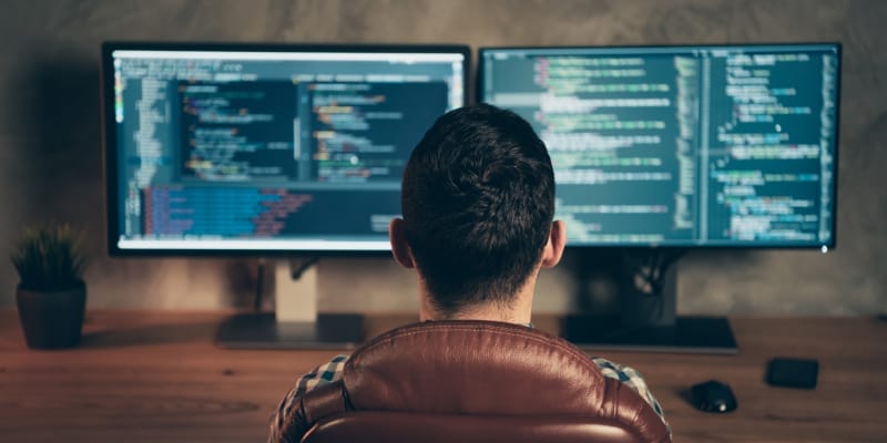 A rear view of a software tester sitting in front of screen at workplace.