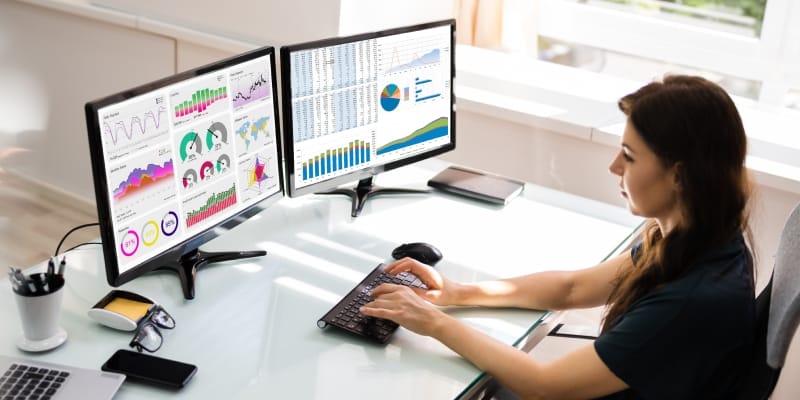 An young woman working with multiple screens illustrate data analytics jobs.