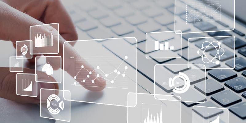 An IT professional working on laptop with virtual data analytics icons.