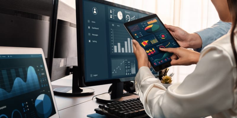 Two analysts comparing data analysis in Power BI vs. Excel on a laptop, with graphs and charts displayed on the screen.